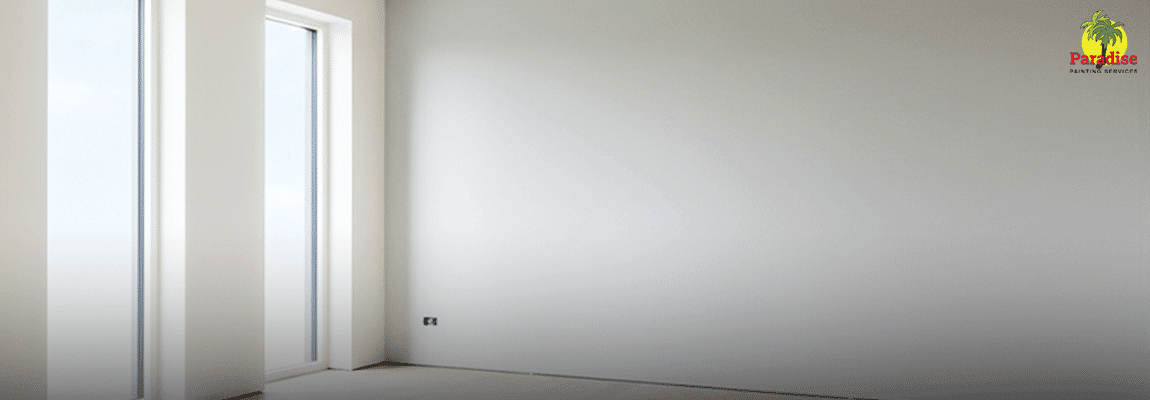 A bright, empty room featuring perfectly smooth, freshly plastered and painted white walls with natural light streaming through large windows.